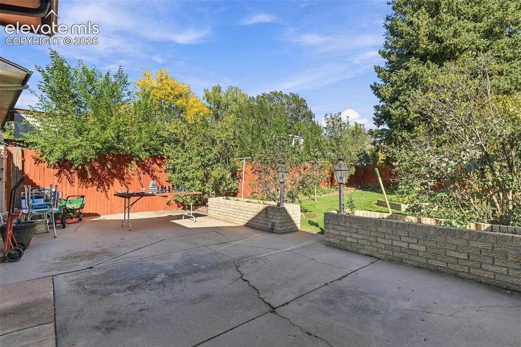 Image 6 of 42: Concrete patio area featuring raised brick planters and privacy fencing