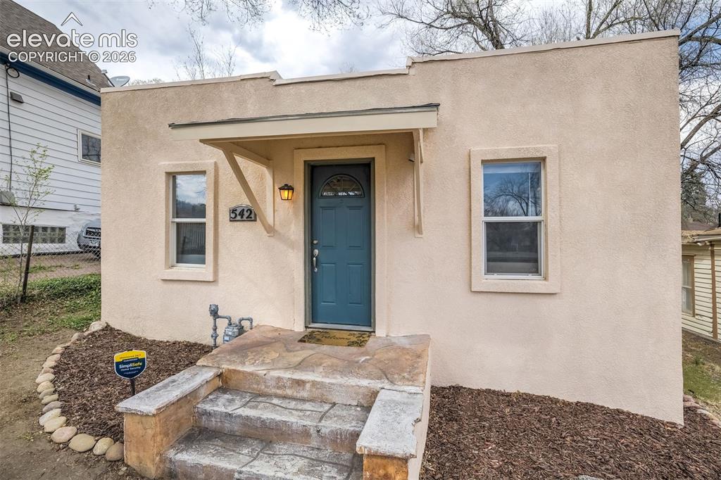 Image 2 of 46: Stucco exterior featuring a teal entry door with glass paneling, a coordina
