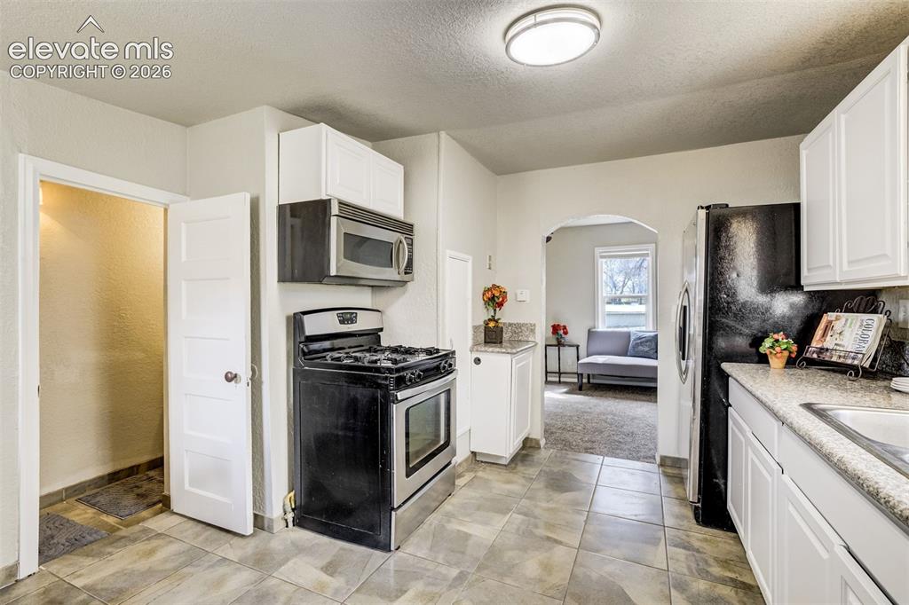 Image 21 of 46: Kitchen featuring white cabinetry, gray countertop surfaces, a black refrig