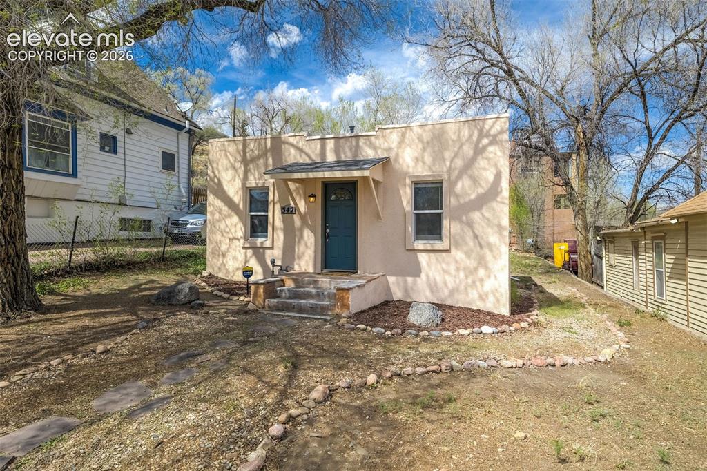 Image 5 of 46: Stucco exterior featuring a covered entry with a teal front door, three sto