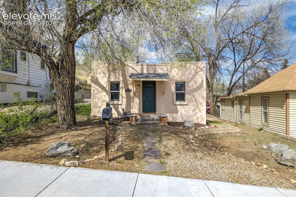 Image 6 of 46: Stucco exterior residence featuring a covered entry, dark-paneled door, and