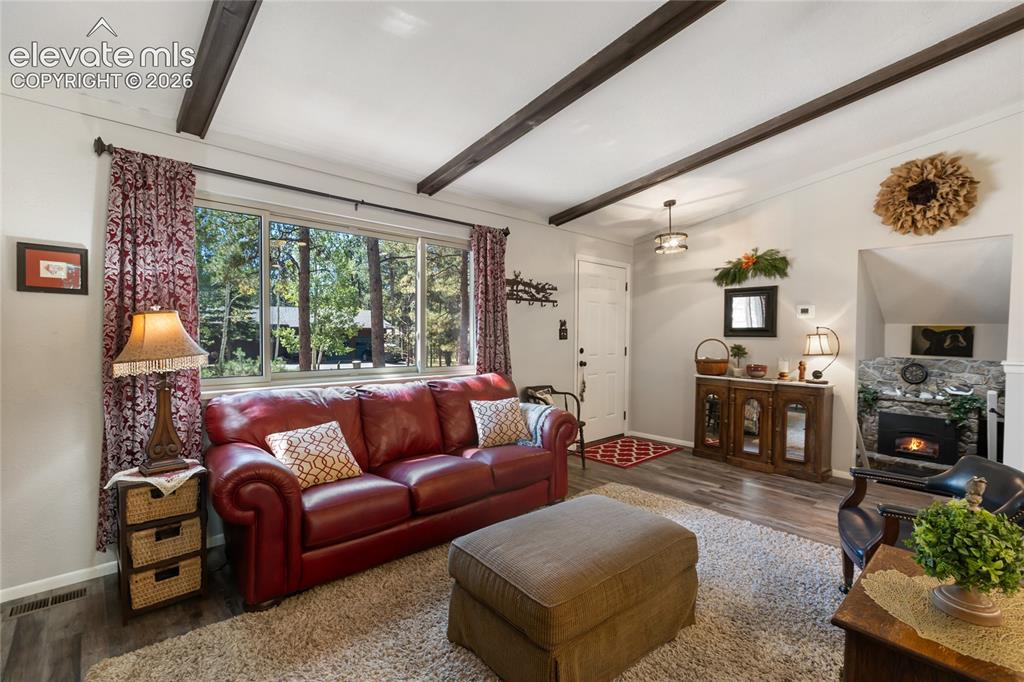 Image 11 of 39: Wood-finish flooring, exposed ceiling beams, a stone fireplace, large windo