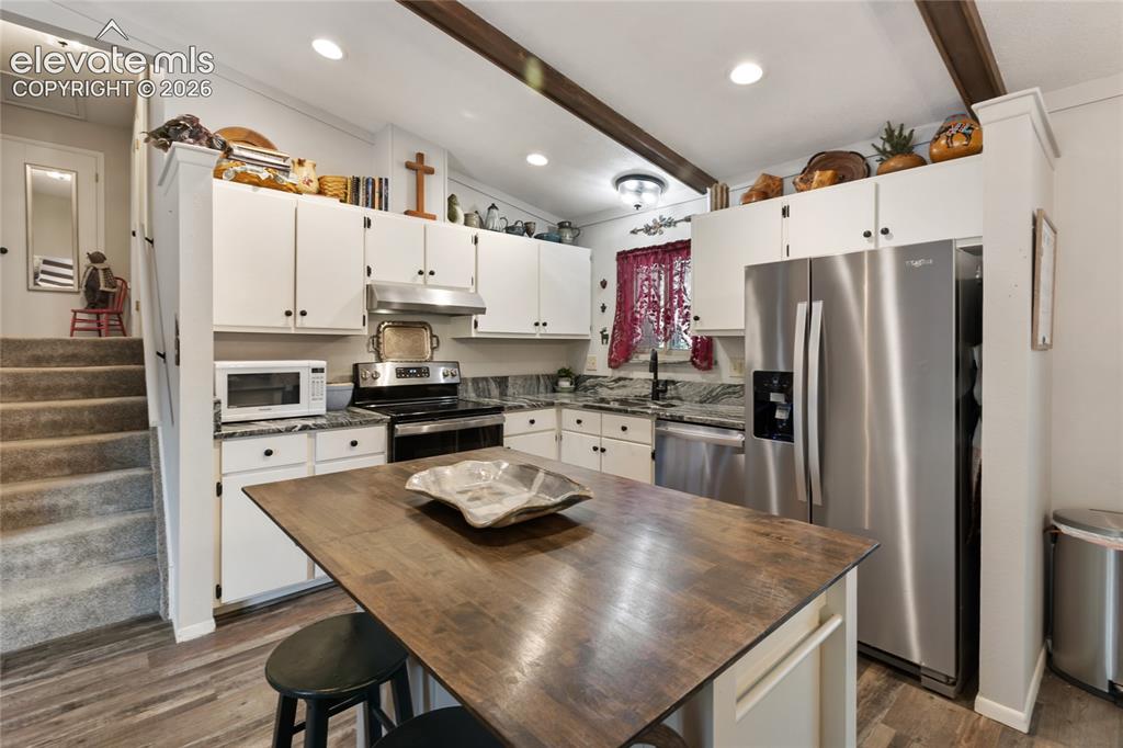 Image 13 of 39: Kitchen featuring white cabinetry, wood-finish flooring, stainless steel ap