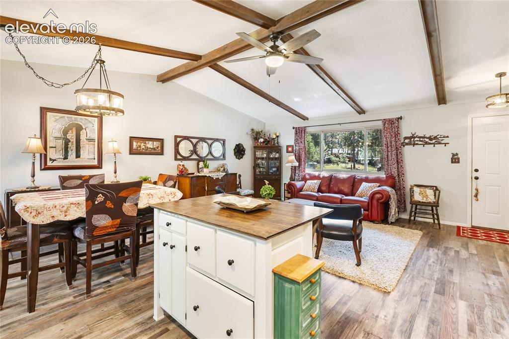 Image 18 of 39: Vaulted ceiling with exposed wood beams, wood-finish flooring, white kitche