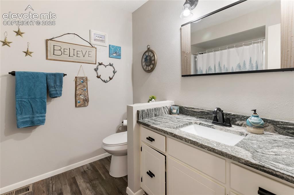 Image 27 of 39: Bathroom featuring wood-finish flooring, a white vanity with panel-front ca
