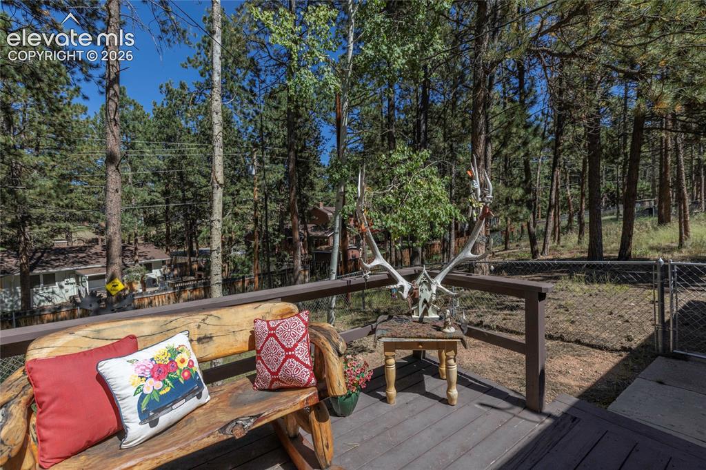 Image 37 of 39: Elevated deck with wood-finish flooring and a natural wood bench, surrounde
