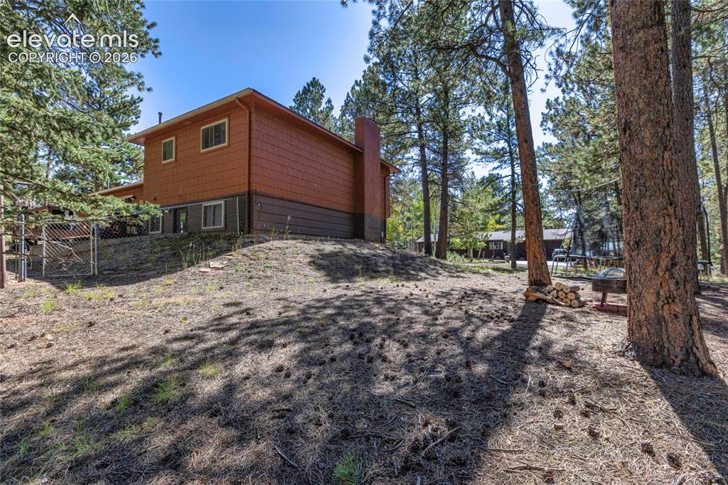 Image 39 of 39: Wood-sided exterior with a natural, sloped landscape featuring mature trees
