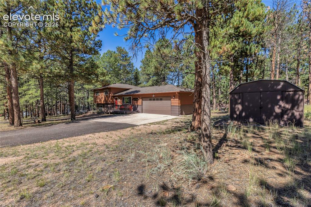 Image 4 of 39: Wood-clad exterior with a brown garage door, surrounded by mature trees