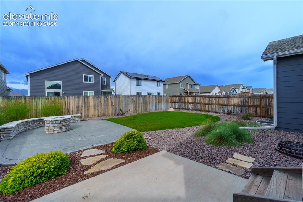 Image 25 of 27: Expansive backyard featuring a stone fire pit, concrete patio, natural wood