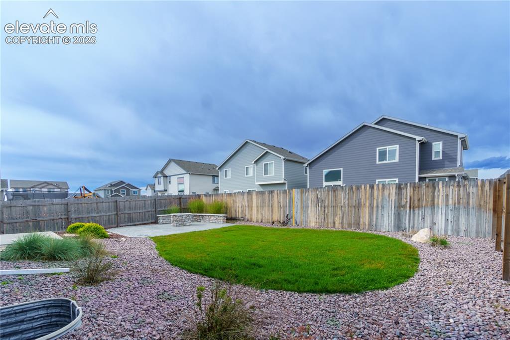 Image 26 of 27: Private backyard featuring a concrete patio, built-in stone fire pit, and a