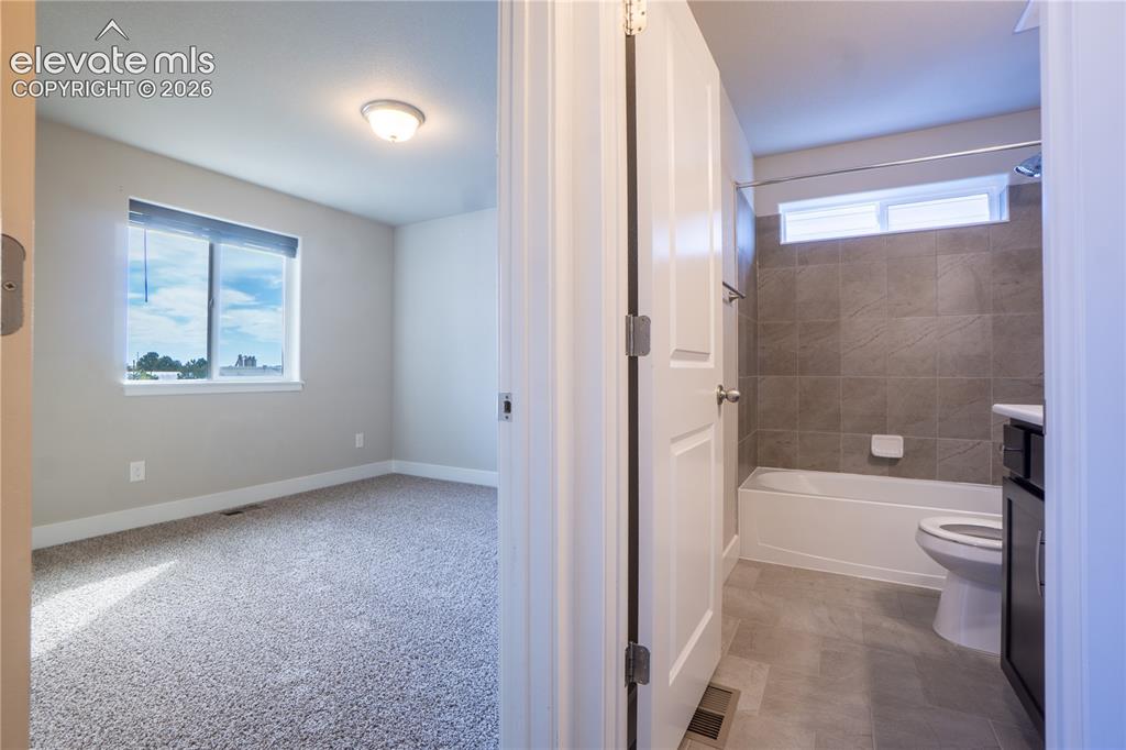 Image 3 of 27: Carpeted room with a large window, accompanied by a bathroom featuring a ti