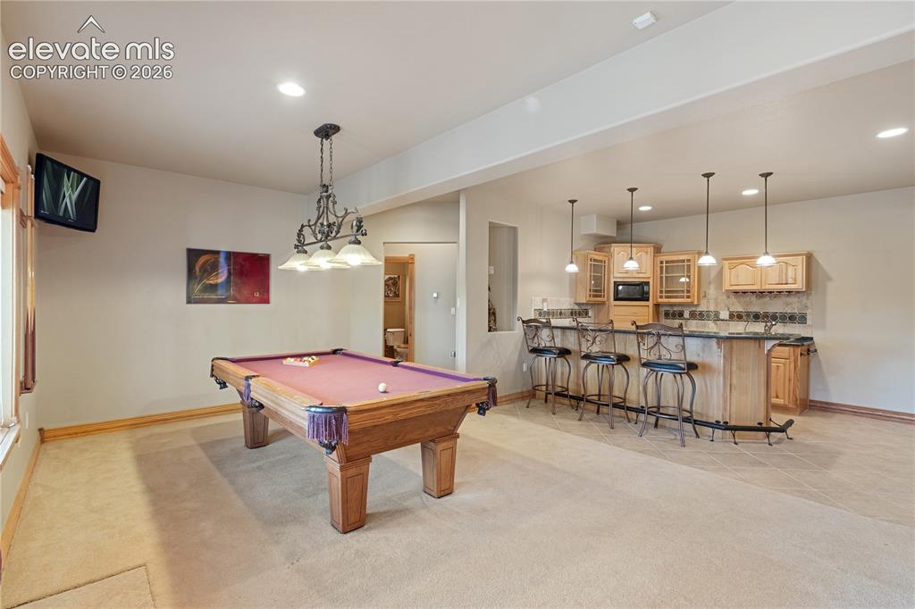Image 30 of 50: Downstairs game room with fireplace and wet bar. Looking toward gym and the