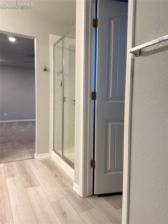 Image 8 of 14: Full bath with wood finished floors, a textured wall, and a shower stall