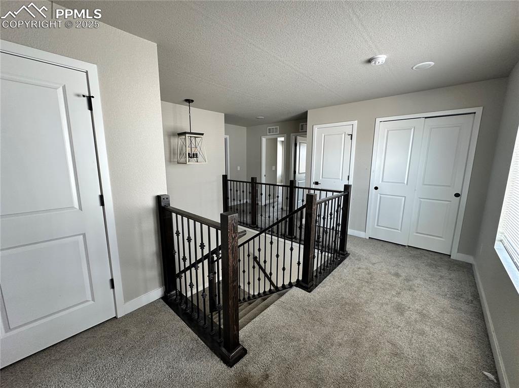 Image 10 of 19: Corridor featuring an upstairs landing, carpet, and a textured ceiling