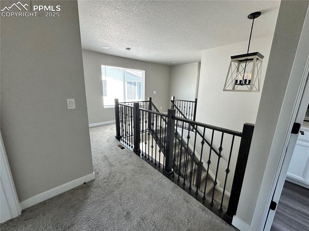 Image 11 of 19: Hall with an upstairs landing, a textured ceiling, and dark colored carpet
