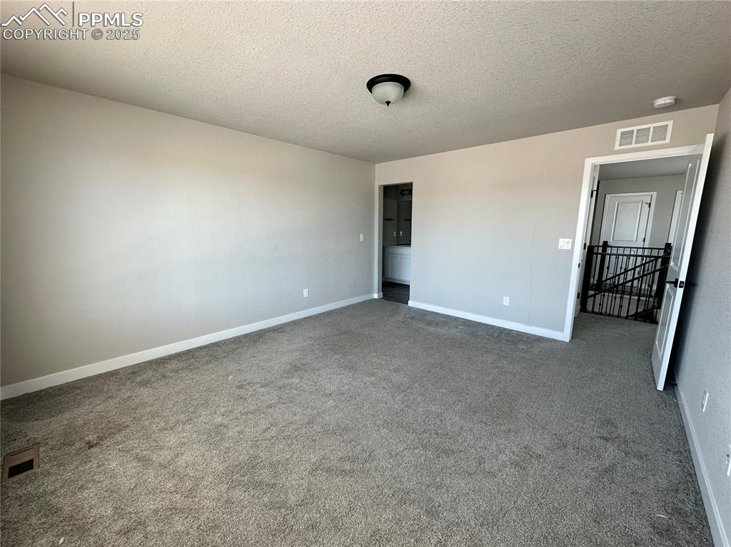 Image 13 of 19: Unfurnished room with dark colored carpet and a textured ceiling
