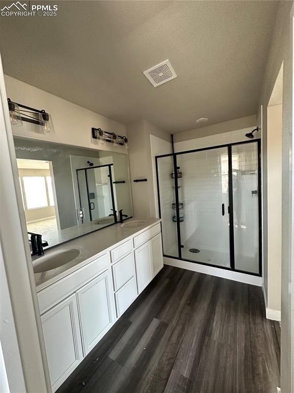 Image 15 of 19: Full bathroom with wood finished floors, double vanity, a textured ceiling,