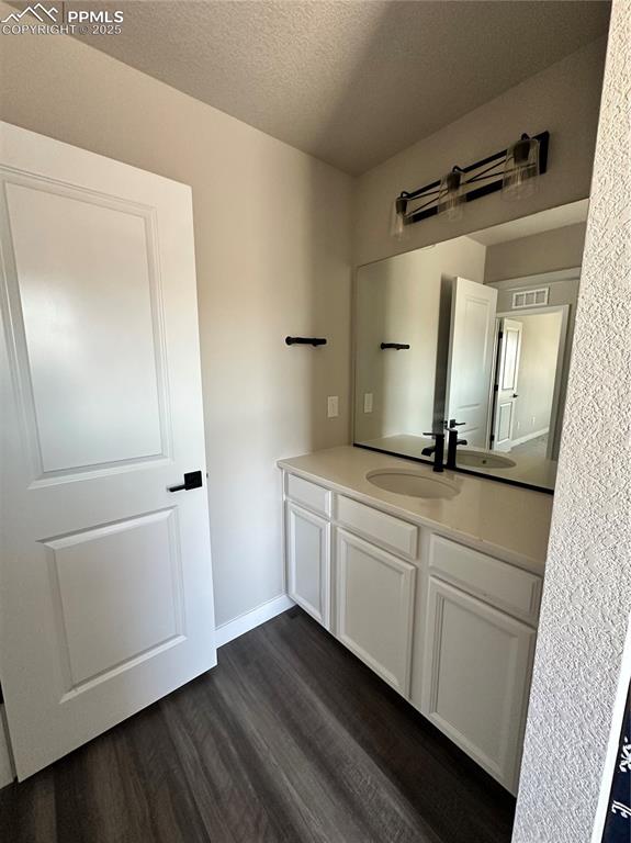 Image 17 of 19: Bathroom with wood finished floors, vanity, and a textured ceiling