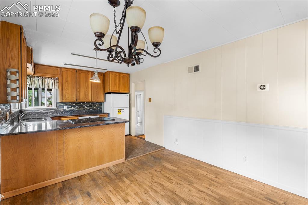 Image 11 of 41: Kitchen with brown cabinetry, a peninsula, tasteful backsplash, dark stone