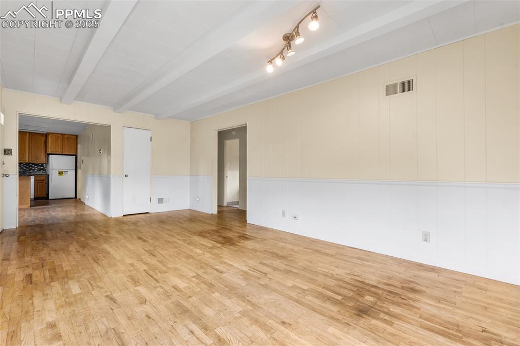 Image 7 of 41: Spare room featuring light wood-style flooring, wainscoting, and beamed cei