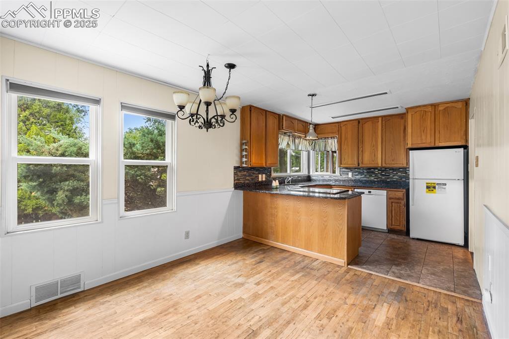 Image 9 of 41: Kitchen with a peninsula, white appliances, dark countertops, wood finished