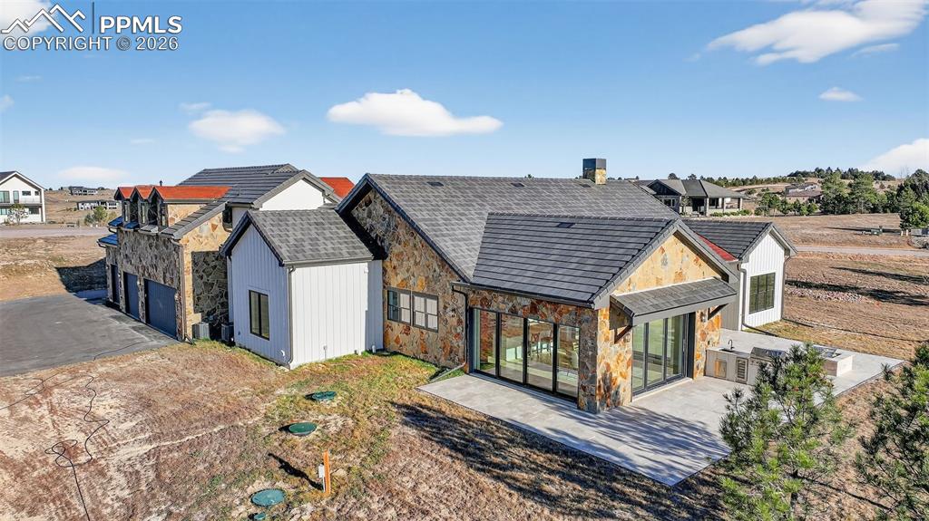 Image 10 of 49: Back of property with stone siding, a patio, a garage, and a residential vi