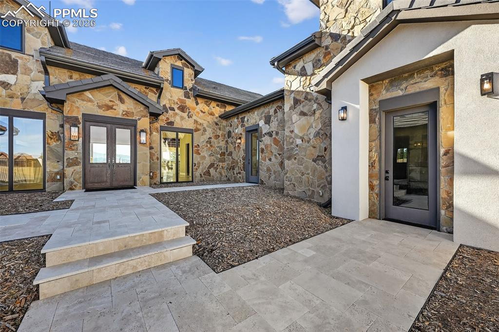 Image 15 of 49: Doorway to property featuring stone siding, french doors, and stucco siding