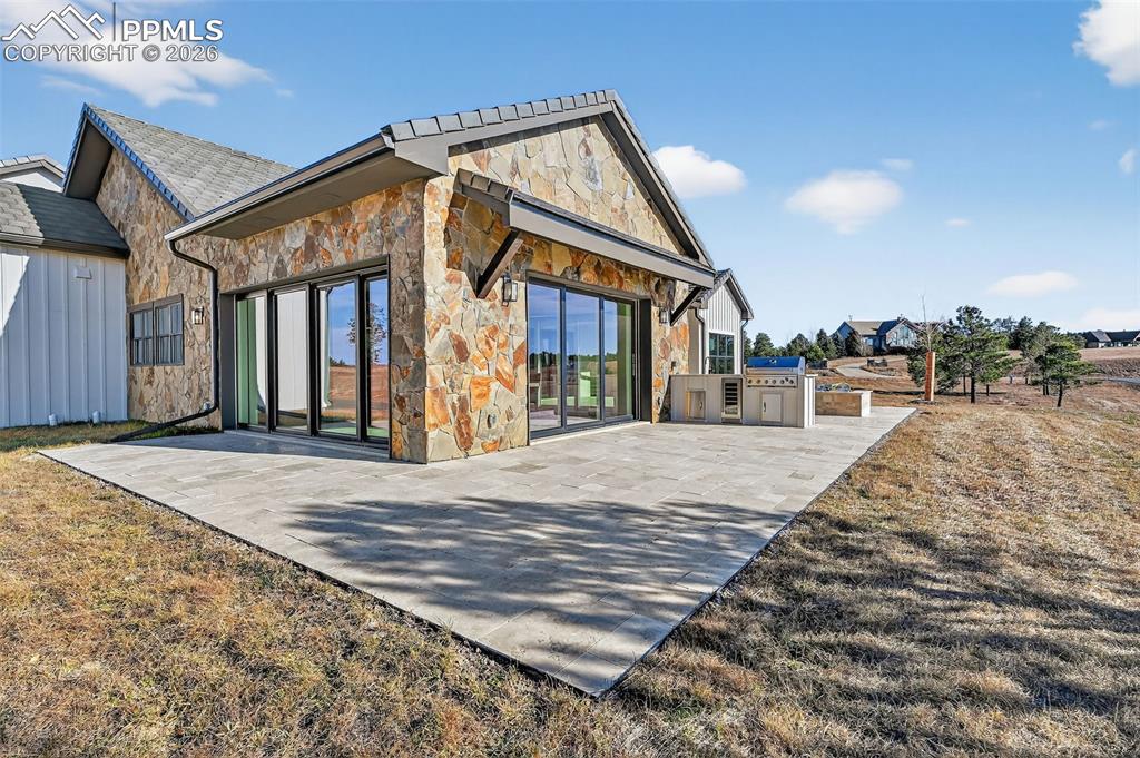 Image 17 of 49: Rear view of house featuring stone siding and an outdoor kitchen
