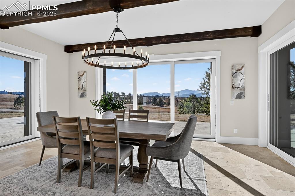 Image 27 of 49: Dining room with a mountain view, stone tile floors, beam ceiling, and susp