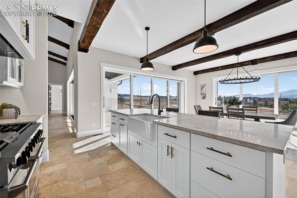 Image 31 of 49: Kitchen featuring white cabinetry, stone tile floors, light stone counterto