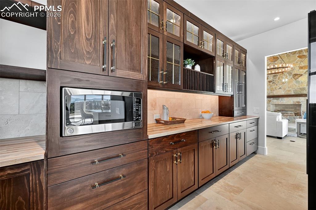 Image 35 of 49: Kitchen featuring stainless steel microwave, glass fronted cabinets, wooden