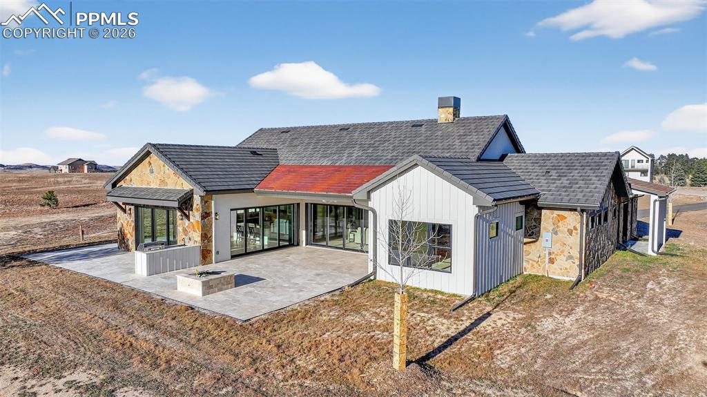 Image 7 of 49: Rear view of house with stone siding, a patio area, and a chimney