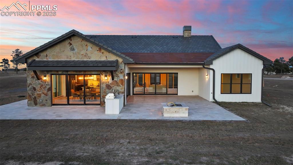 Image 9 of 49: Back of property featuring stone siding, a chimney, and a patio area