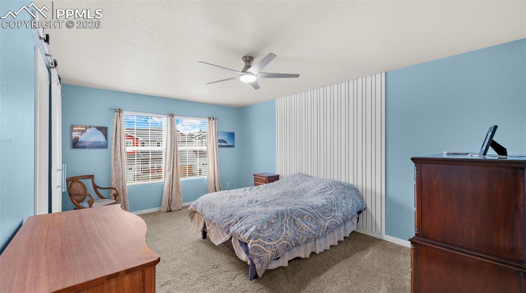 Image 18 of 43: Bedroom with carpet flooring, a ceiling fan, and a barn door