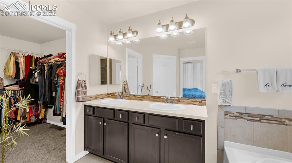 Image 19 of 43: Ensuite bathroom with backsplash, double vanity, a walk in closet, light ca
