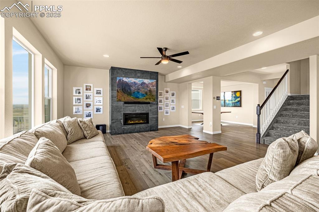 Image 17 of 46: Living area with stairs, ceiling fan, wood finished floors, a tile fireplac