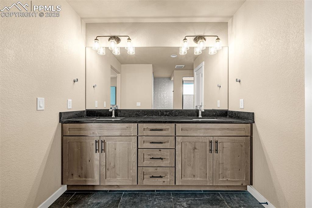 Image 26 of 46: Full bathroom featuring a textured wall, double vanity, and dark tile patte