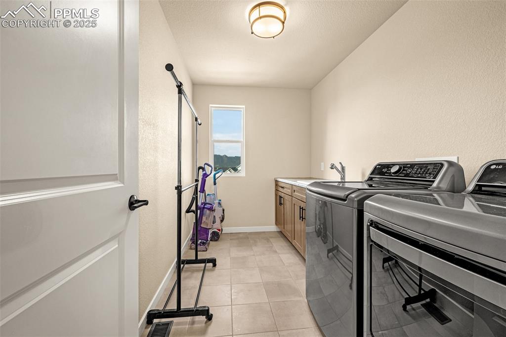 Image 31 of 46: Laundry room with washer and dryer, light tile patterned flooring, cabinet