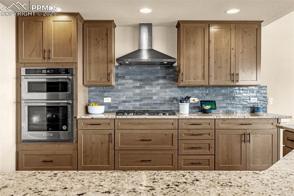 Image 7 of 46: Kitchen featuring light stone countertops, stainless steel appliances, wall