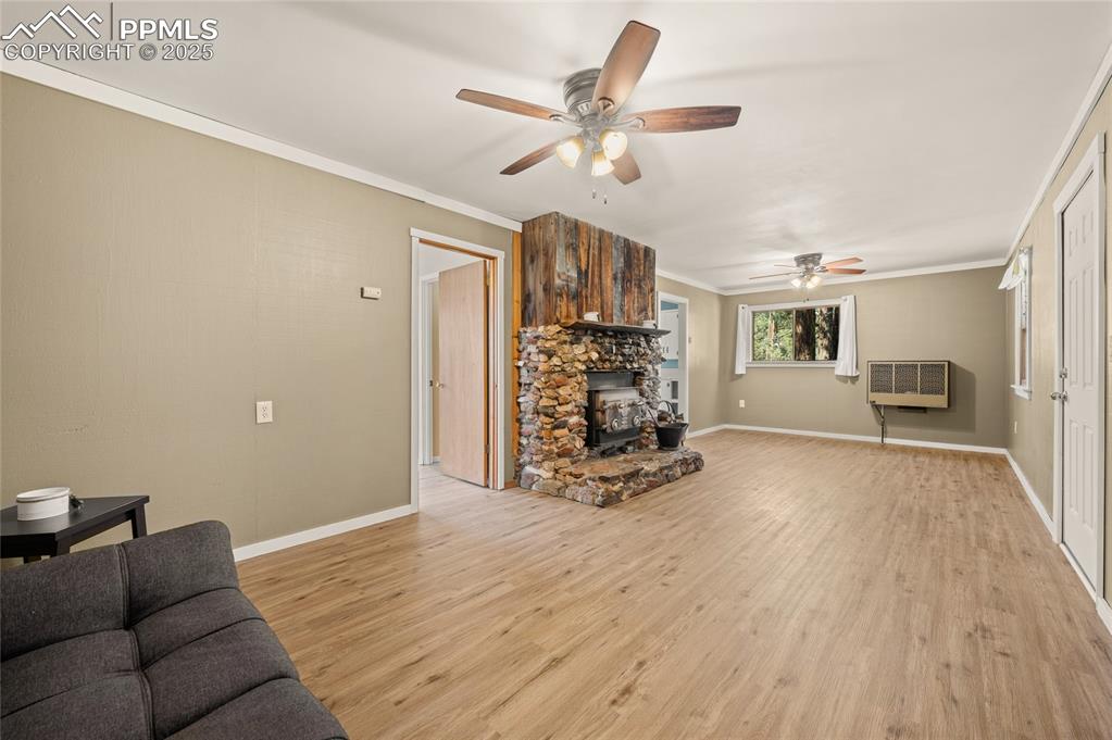 Image 16 of 27: Living area featuring a wood stove, ceiling fan, ornamental molding, light