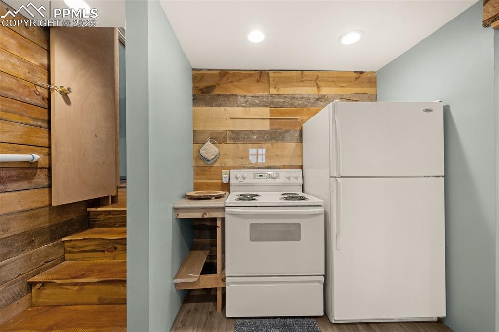 Image 9 of 27: Kitchen featuring white appliances, wooden walls, wood finished floors, and