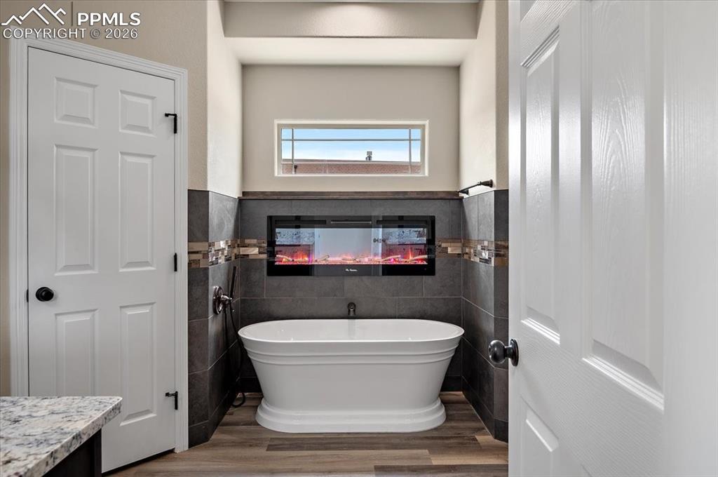 Image 26 of 45: Bathroom with tile walls, wood finished floors, a freestanding tub, wainsco