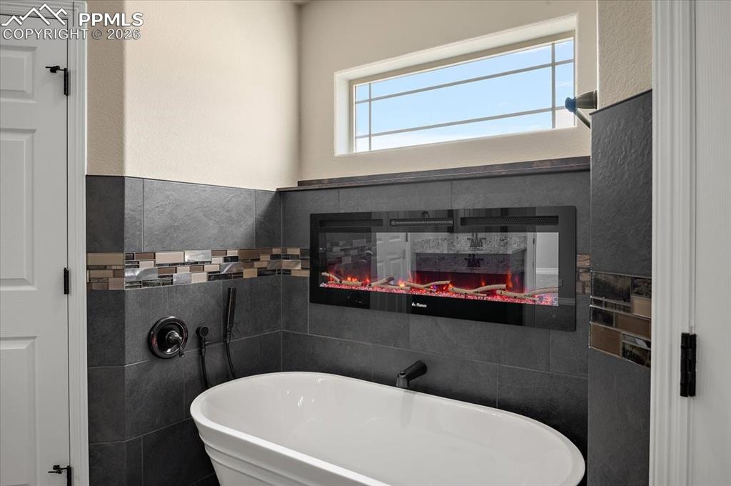 Image 30 of 45: Bathroom with tile walls, a freestanding bath, and a multi sided fireplace