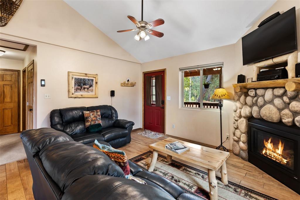 Image 12 of 36: Vaulted ceiling with a ceiling fan, wood-finish flooring, stone-clad firepl