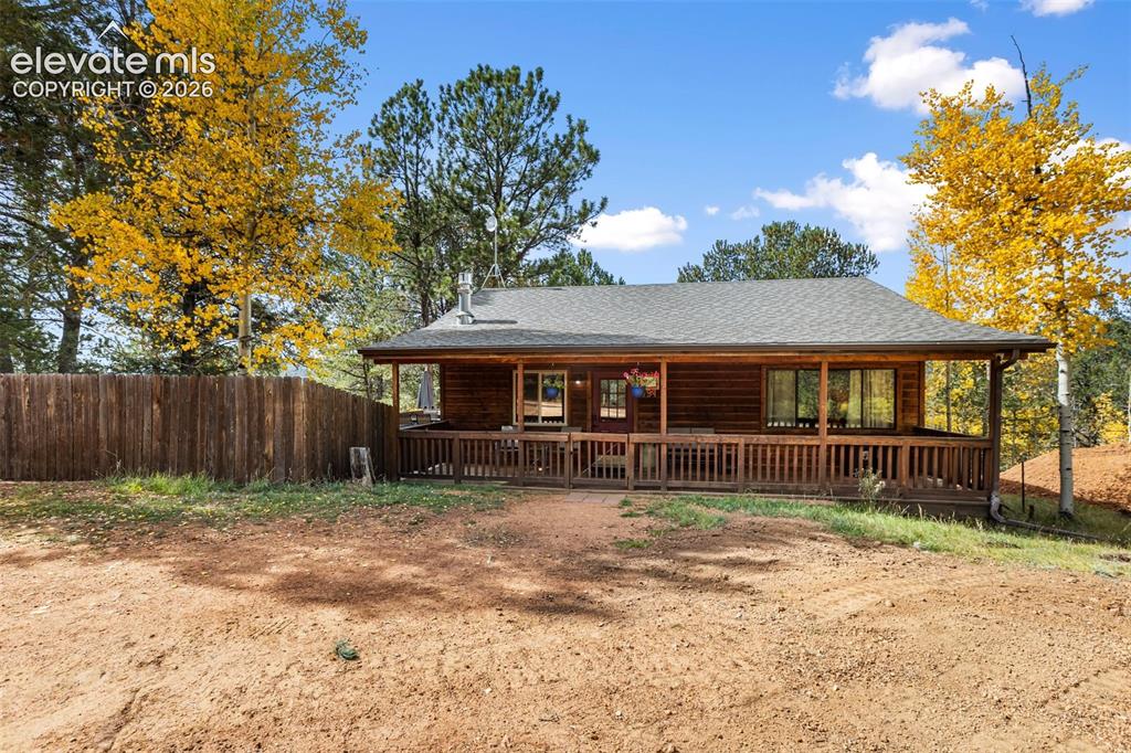 Image 2 of 36: Log cabin exterior featuring a wide covered porch, wood plank railing, and