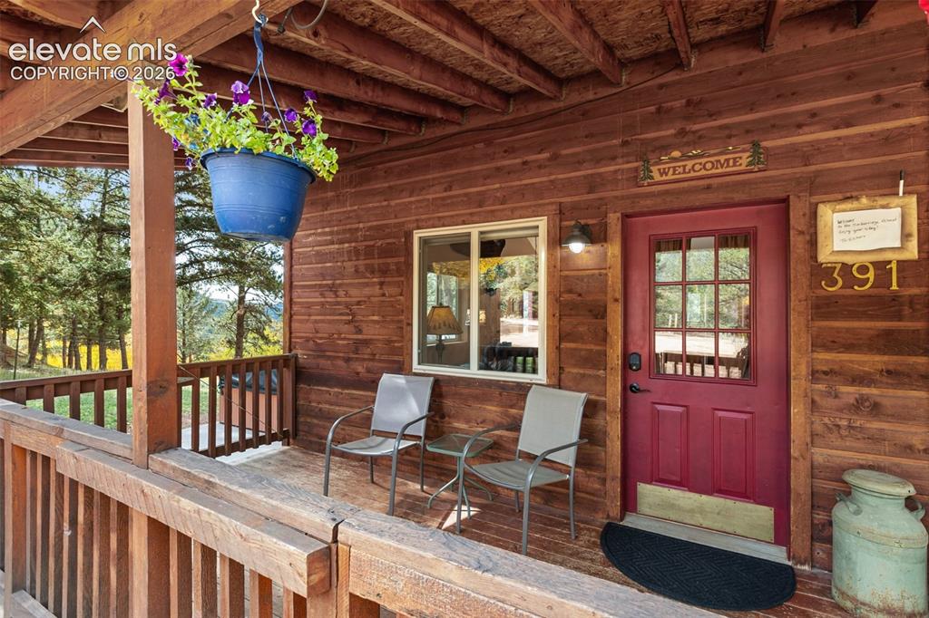 Image 3 of 36: Covered front porch with wood-finish siding, a red entry door with glass pa