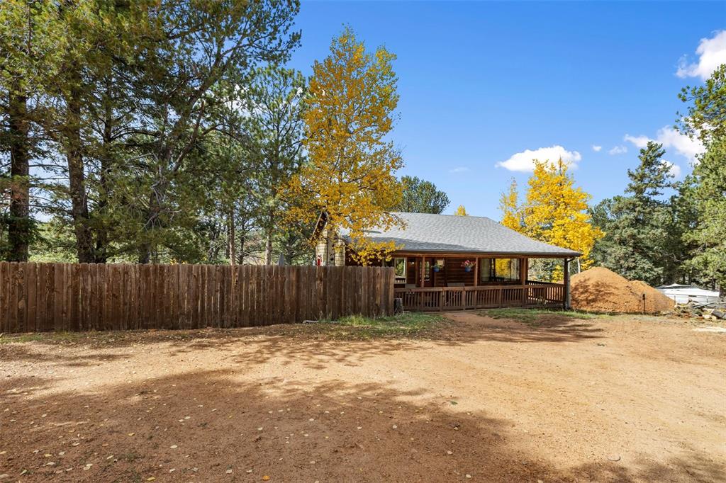 Image 34 of 36: Log cabin exterior with a covered front porch, wood railing, and shingle ro
