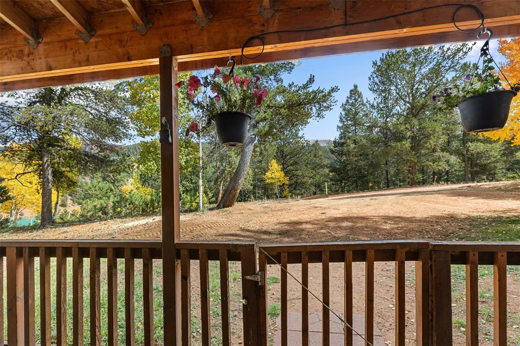 Image 4 of 36: Covered porch with exposed wood beams, wood railing, and a natural landscap