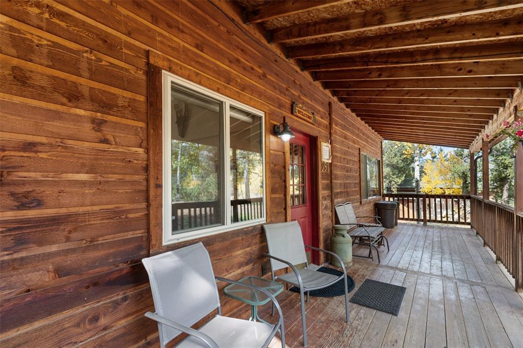 Image 5 of 36: Expansive wood-plank covered porch with a red entry door