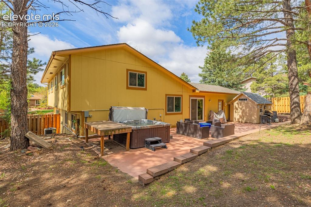 Image 27 of 40: Expansive concrete patio featuring a hot tub with steps, a wood-sided utili